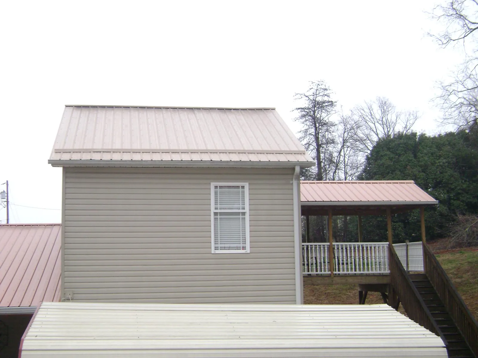 Tan metal roofs on a two story addition and attached porch, from a Roof Replacement job in Jamesville